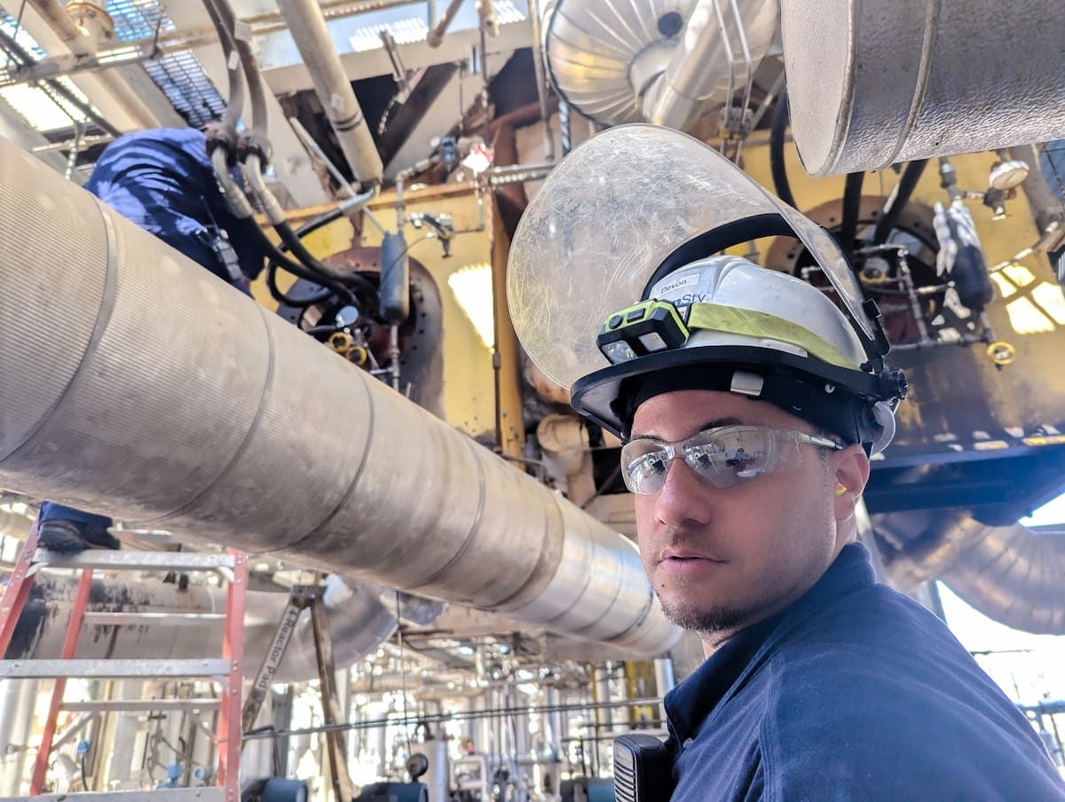 A man in a hardhat and safety glasses examines equipment